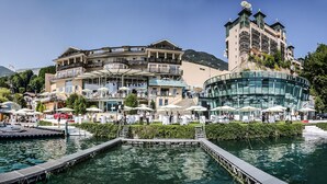 A waterfront hotel with multiple balconies, outdoor seating, and boats docked. - Scalaria Sunset Wing (Sankt Wolfgang im Salzkammergut)