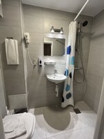 Un baño con inodoro, lavamanos, espejo, ducha y toallero.