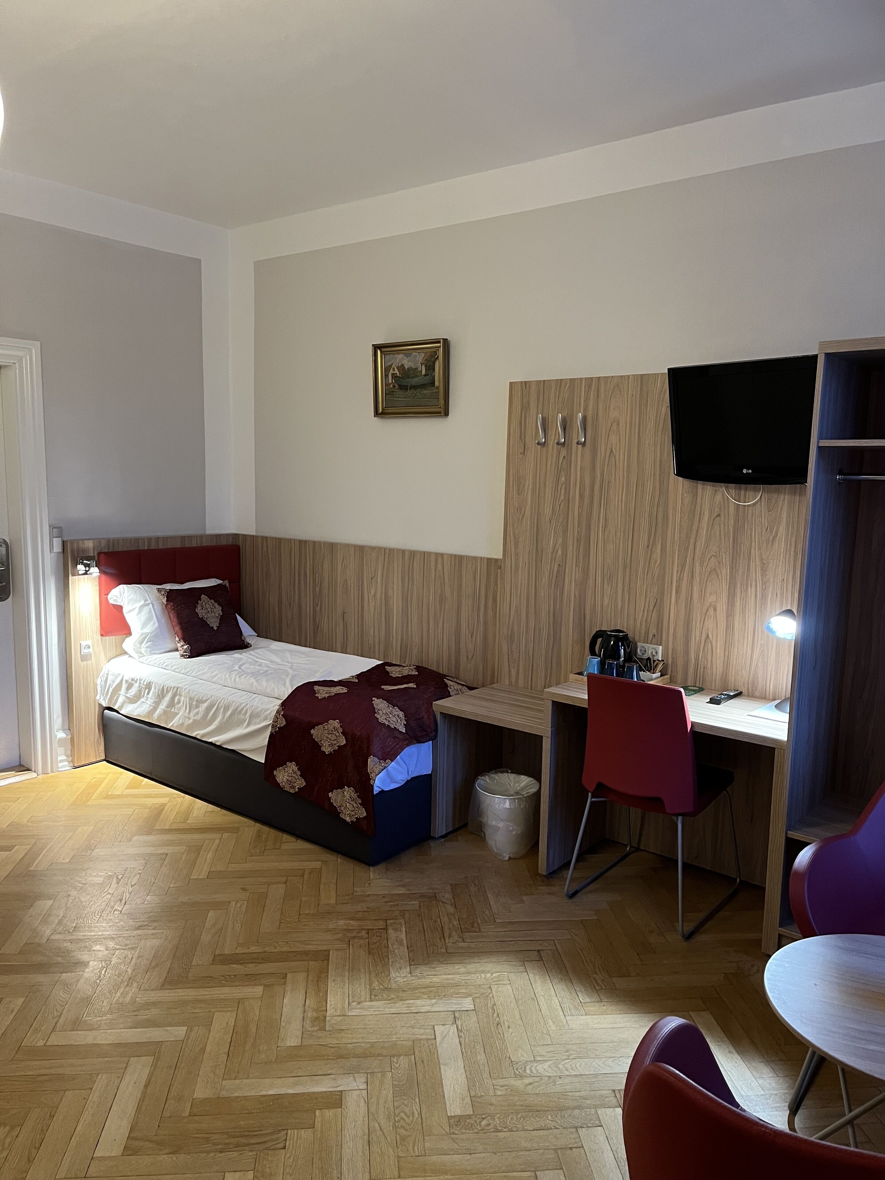Un dormitorio con cama, escritorio, silla, televisor y cubo de basura.