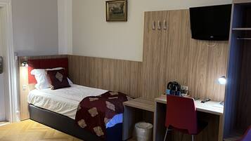 A bedroom with a bed, a desk, a chair, a TV, and a waste bin.