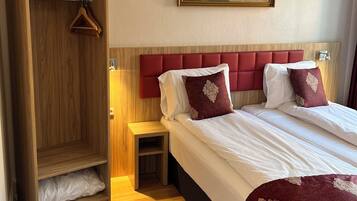 A hotel room with a wooden wardrobe, a bed with red headboard, white bedding, and a painting of a landscape on the wall.