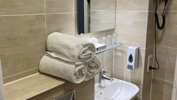 Un baño con azulejos color beige, un lavabo, un espejo, un perchero para toallas, un secador de pelo y un dispensador de jabón.