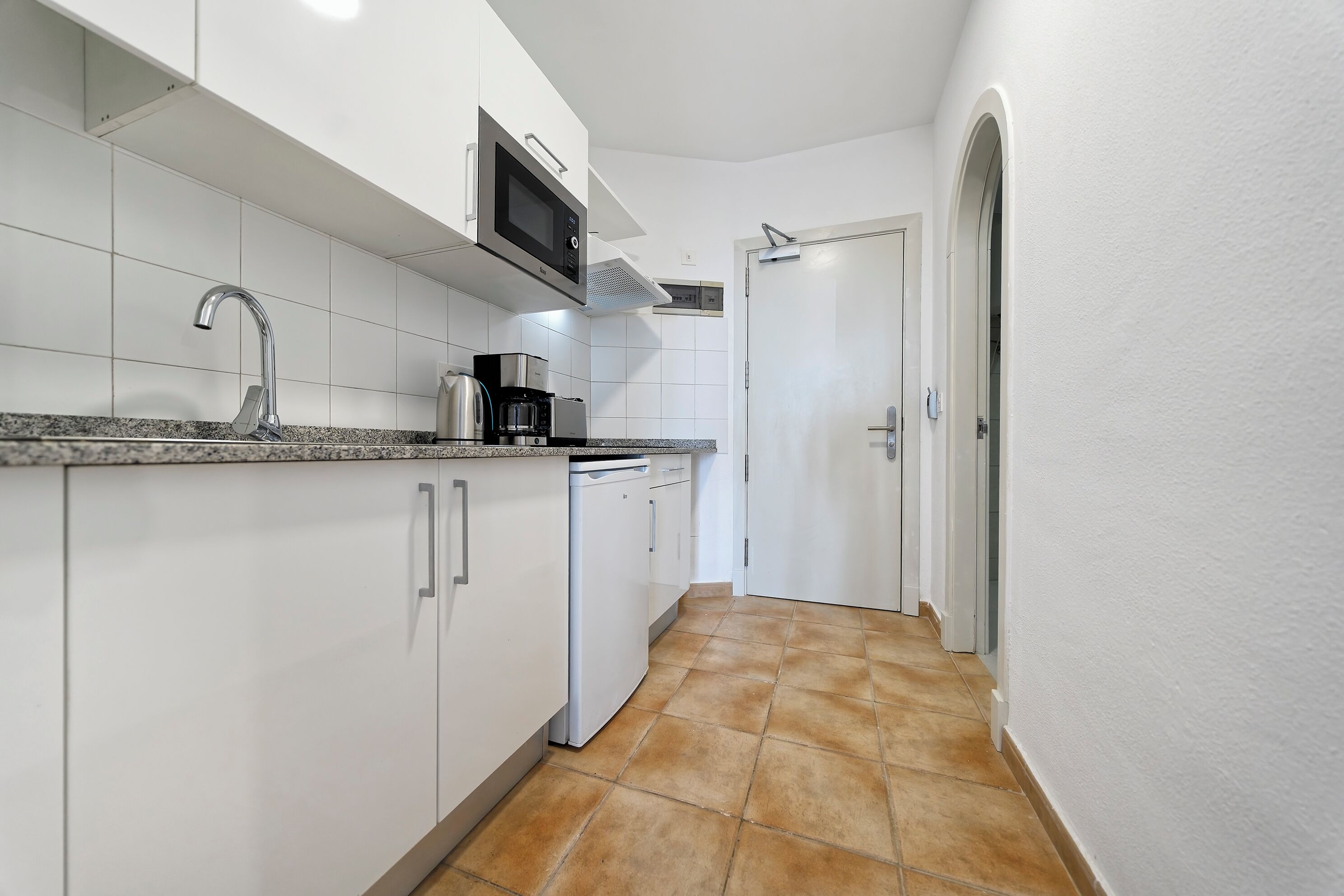 Una cocina moderna con armarios blancos, encimera de granito, pileta de acero inoxidable, microondas, cafetera y lavavajillas.