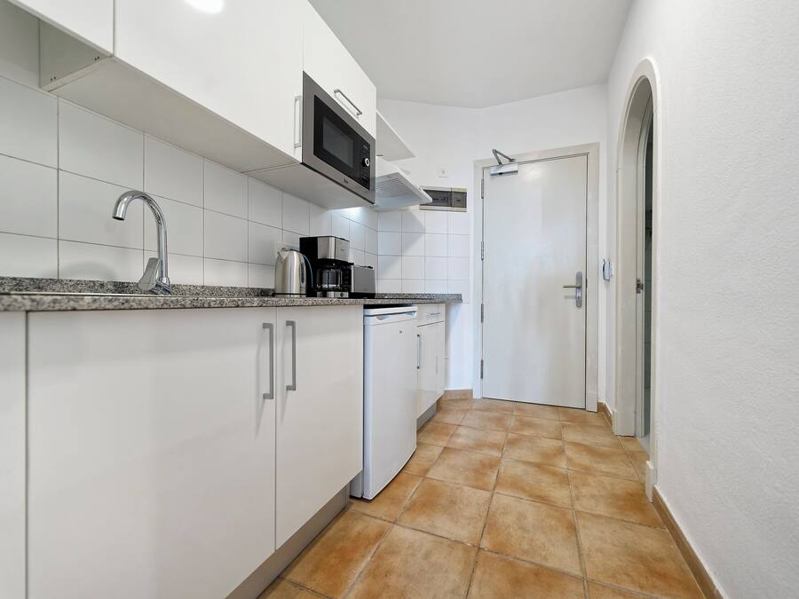 Una cocina moderna con armarios blancos, encimera de granito, pileta de acero inoxidable, microondas, cafetera y lavavajillas.