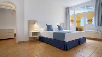 Un dormitorio con cama, mesitas de noche, armario y ventana con cortinas.