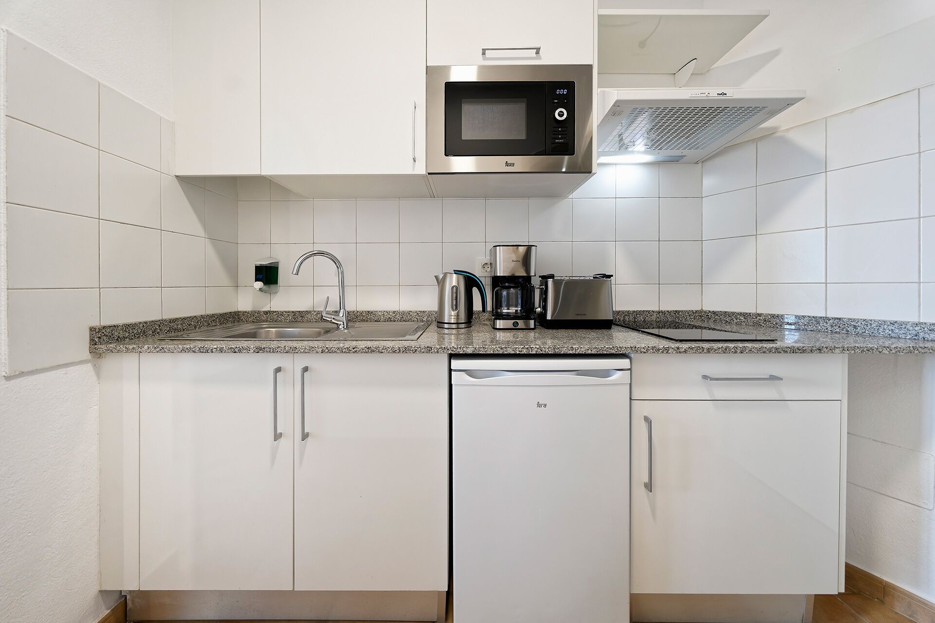 A modern kitchen with white cabinets, a stainless steel microwave, a coffee maker, and a dishwasher.