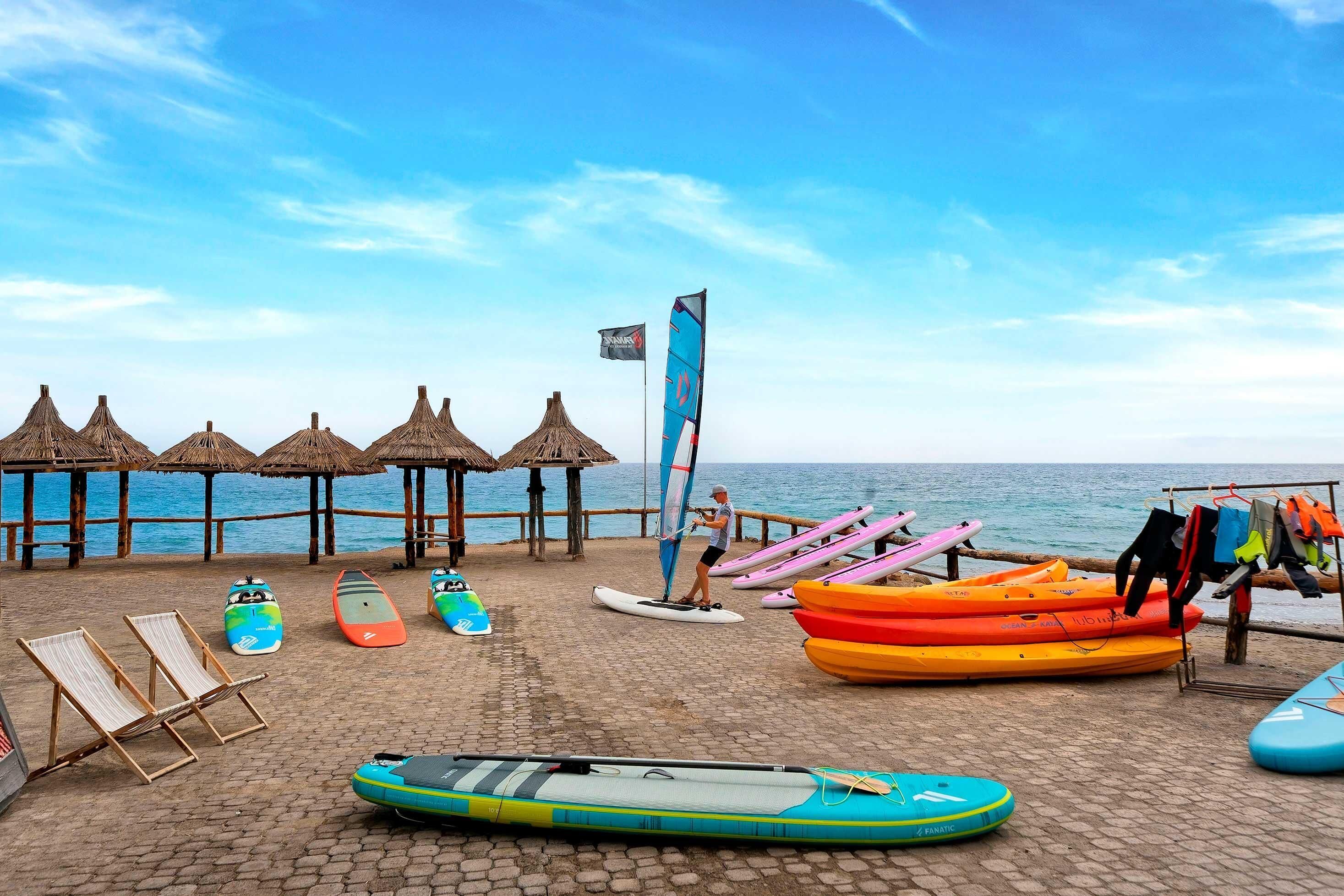 Una playa con sombrillas de paja, tablas de remo y kayaks.