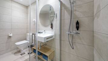 Et moderne badeværelse med brusekabine i glas, toilet, vask og spejl.