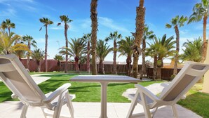 An outdoor patio with a white table and two chairs, surrounded by palm trees and a well-maintained lawn. - Sport Hotel Monte Feliz - powered by Playitas (San Bartolomé de Tirajana)