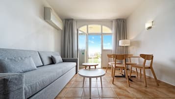 A modern living room with a grey sofa, a round white table, and two wooden chairs.