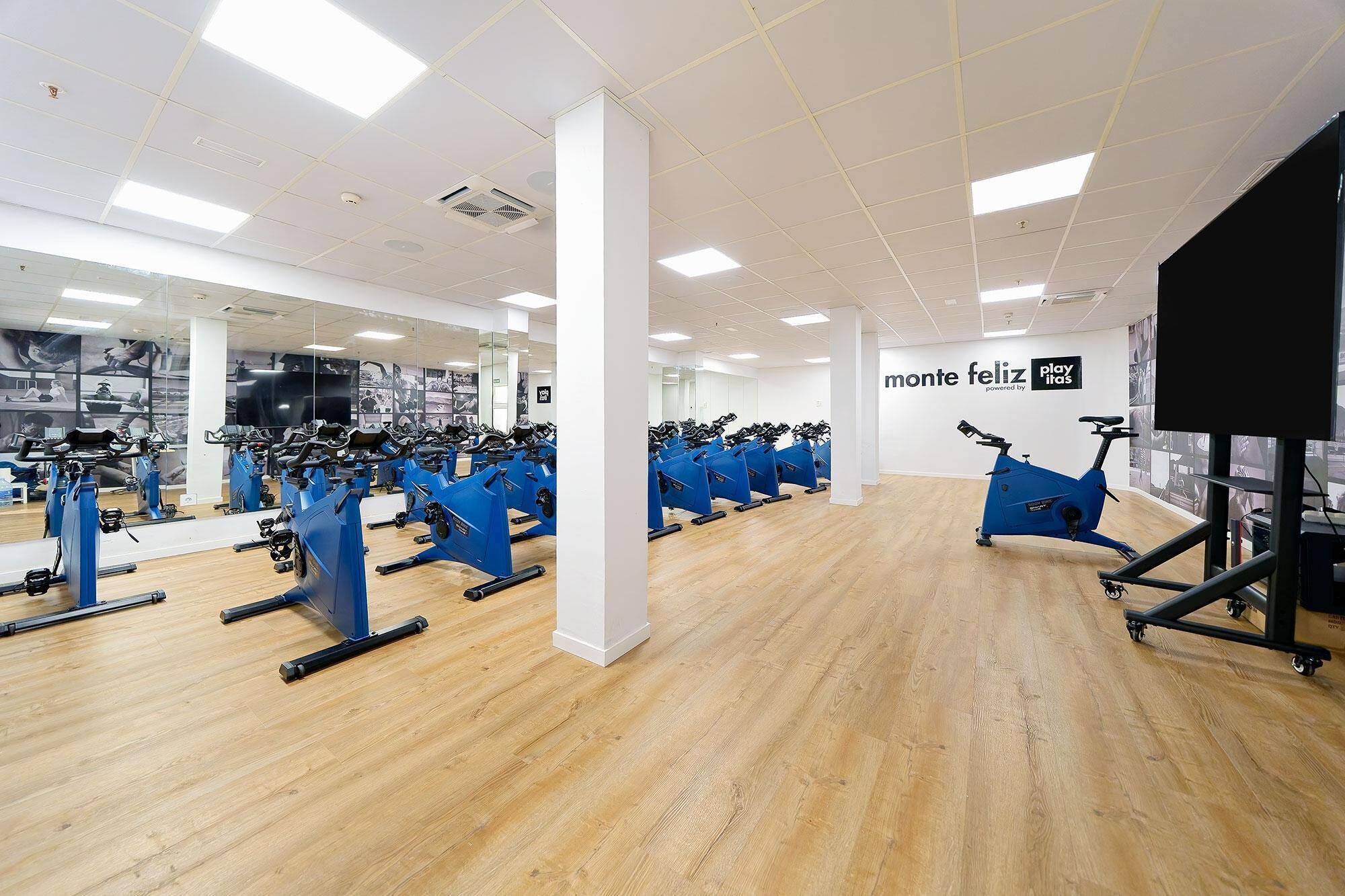 Un gimnasio con varias bicicletas estáticas, suelo de madera y espejos en las paredes.