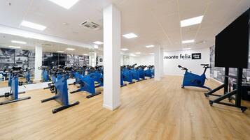Un gimnasio con varias bicicletas estáticas, suelo de madera y espejos en las paredes.