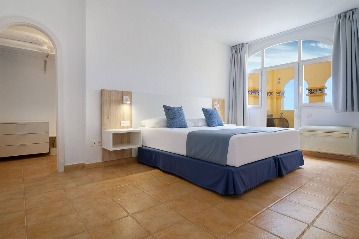 A bedroom with a bed, bedside tables, a wardrobe, and a window with curtains.