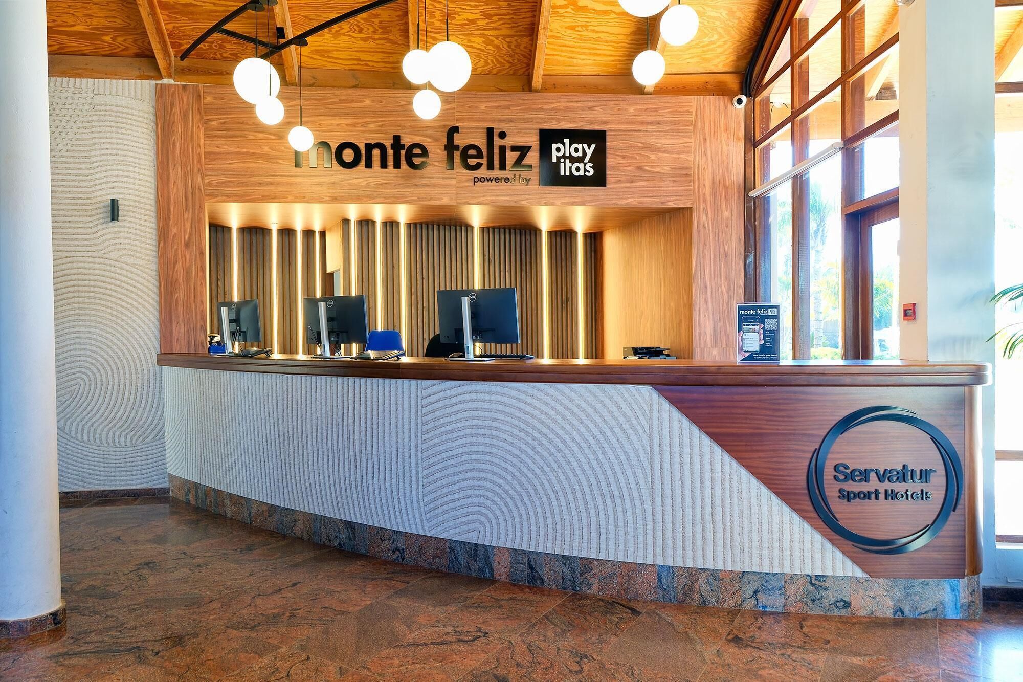 A reception desk with a wooden finish, multiple computer monitors, and a sign reading "Servatür Sport Hotels".