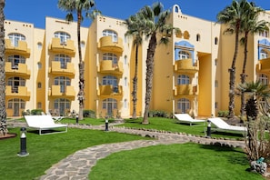 A hotel with yellow exterior walls, multiple balconies, and a well-maintained lawn with lounge chairs.
