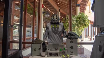 Un maniquí con casco y una camiseta con la palabra "FOX" en la espalda, frente a una exhibición de zapatos y accesorios.