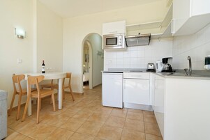 A compact kitchen with white cabinets, a microwave, a coffee maker, and a small refrigerator.