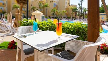 A poolside table with two drinks, a pool, and lounge chairs in a resort setting.