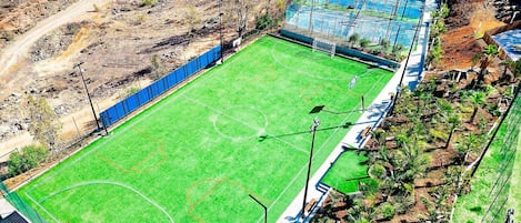 Vista aérea de un campo deportivo con una valla perimetral, un camino de tierra y vegetación escasa.