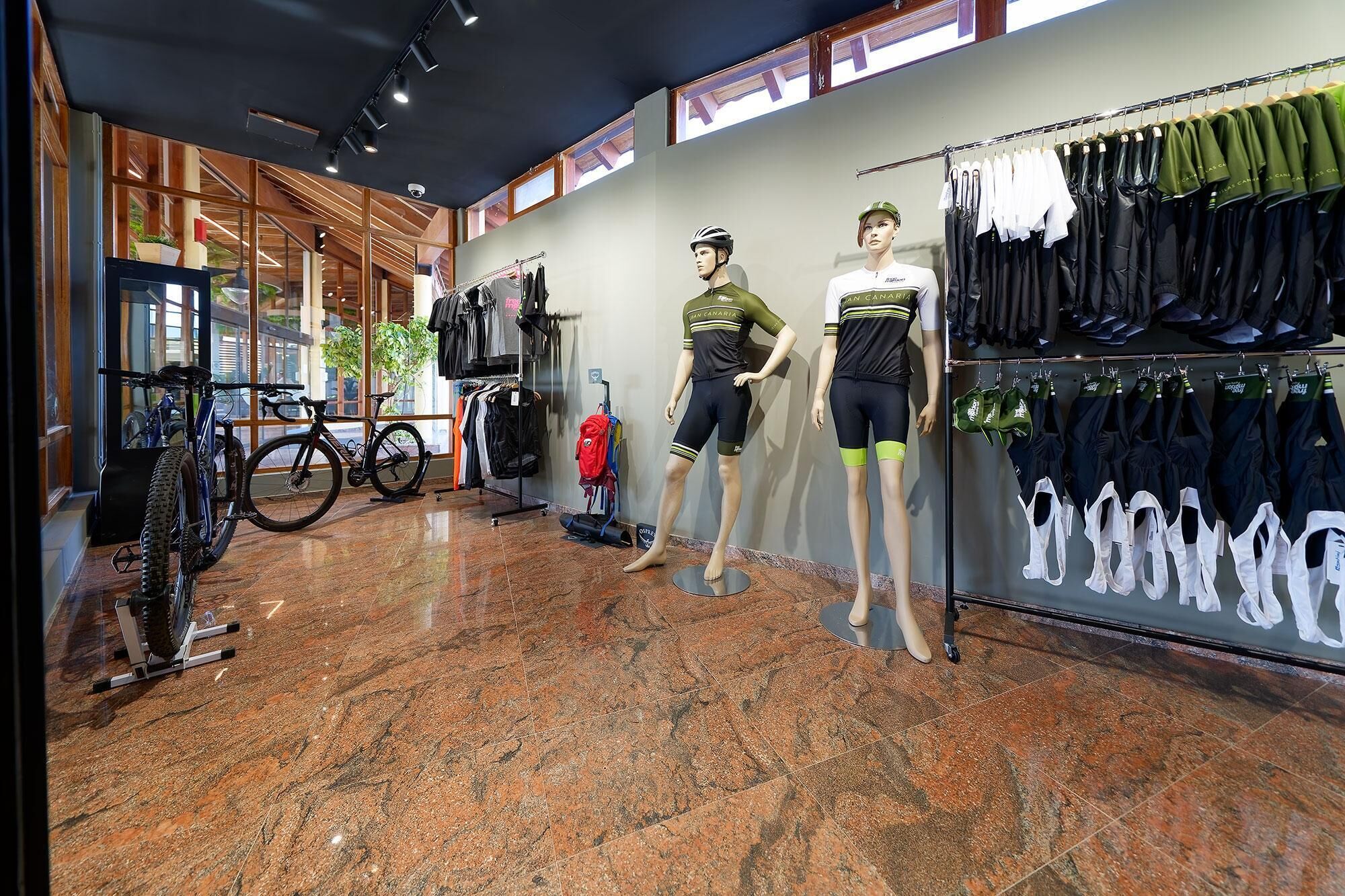 A retail store with mannequins displaying cycling gear, a bike rack, and a variety of clothing items.