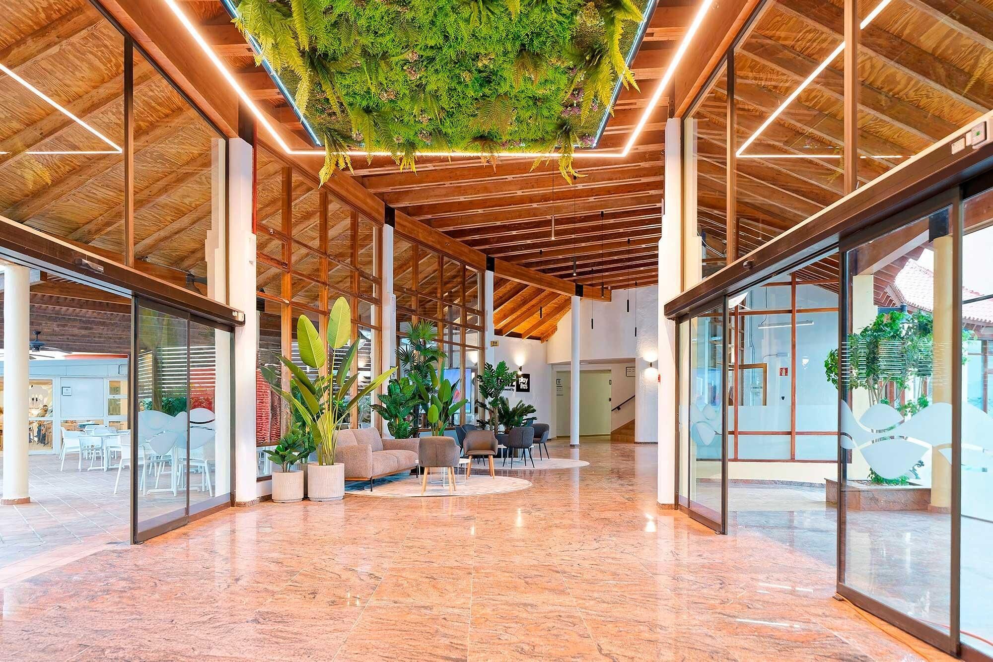 Un hall d’entrée spacieux avec un plafond haut, des poutres en bois et une installation végétale suspendue.