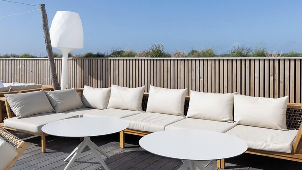 A wooden deck with a sofa and two round tables, a wooden fence, and a clear sky. - Relais Thalasso île de Ré - Hôtel Atalante (Sainte-Marie-de-Re)