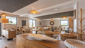 Un espace repas moderne avec des tables et des chaises en bois, des luminaires suspendus et un îlot central agrémenté d’un élément décoratif blanc.