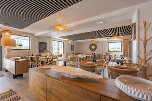 Un comedor moderno con mesas y sillas de madera, iluminación colgante y una isla central con un detalle decorativo blanco.