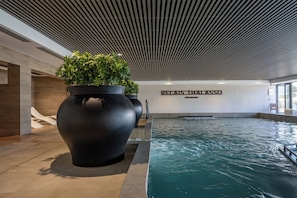 A modern indoor pool area with large planters, a sign reading 'RELAIS THALASSO,' and a wooden ceiling.