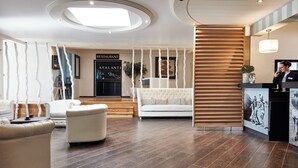 Un hall d’hôtel moderne avec un comptoir d’accueil, un canapé blanc et une cloison en lattes de bois.