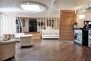 Un moderno vestíbulo de hotel con una recepción, un sofá blanco y un separador de madera con listones.