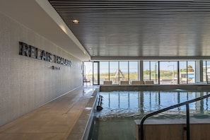 A swimming pool with a view of the beach, a lounge area with chairs, and a sign reading 'RELAIS THALASSO.'
