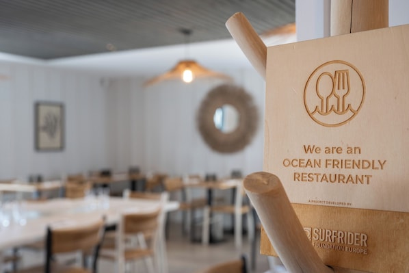 A restaurant interior with wooden tables and chairs, a hanging light fixture, and a sign stating it is an ocean-friendly restaurant.