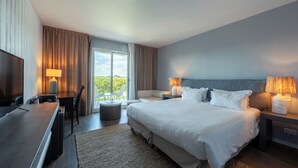 Une chambre d’hôtel comprenant un lit, des lampes de chevet, un bureau avec une lampe, une télévision et une vue sur l’extérieur.