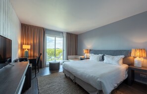 Habitación de hotel con cama, lámparas de noche, escritorio con lámpara, televisor y vistas al exterior.