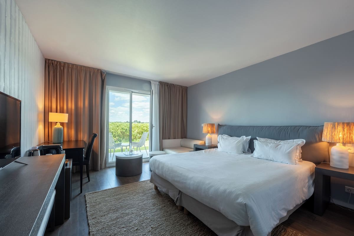 Habitación de hotel con cama, lámparas de noche, escritorio con lámpara, televisor y vistas al exterior.
