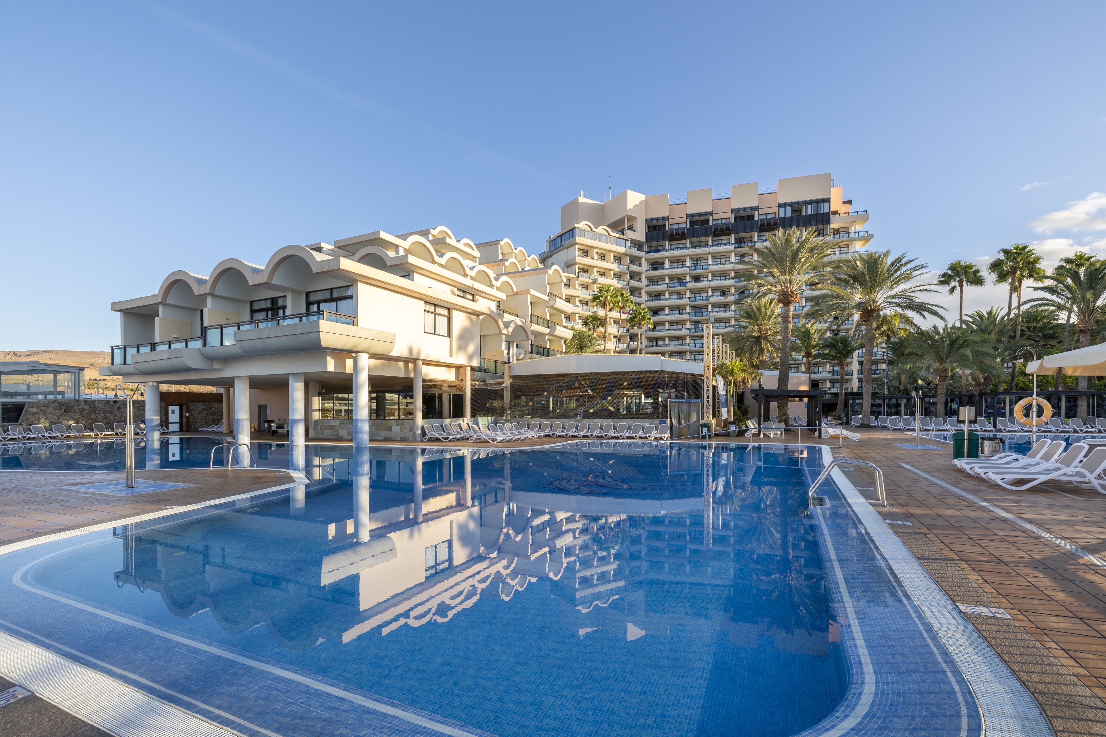 Una piscina con sillas de descanso y un moderno edificio de hotel al fondo.