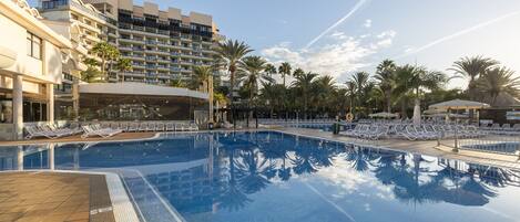 Ein Pool mit Liegestühlen und Palmen, umgeben von Hotelgebäuden.