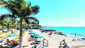 Une plage avec des transats et des parasols, un escalier en bois menant à la plage, et un ciel bleu dégagé.