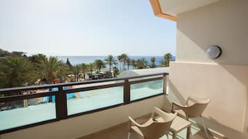 Un balcon avec vue sur la plage et les palmiers. On y trouve deux chaises et une table.