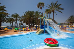 Una piscina con tobogán de agua, sillas de descanso y palmeras.