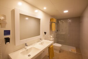 A modern bathroom with a large mirror, two sinks, a toilet, and a glass-enclosed shower.