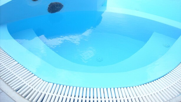 Una piscina azul cristalina con borde de cubierta blanco y algunas rocas.