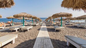 Ein Strand mit einer Holzpromenade, die zu Liegestühlen unter Reetdachschirmen führt.