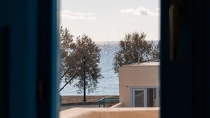Blick durch eine offene Tür auf einen Balkon mit Blick auf einen Strand, Bäume und einen klaren Himmel.