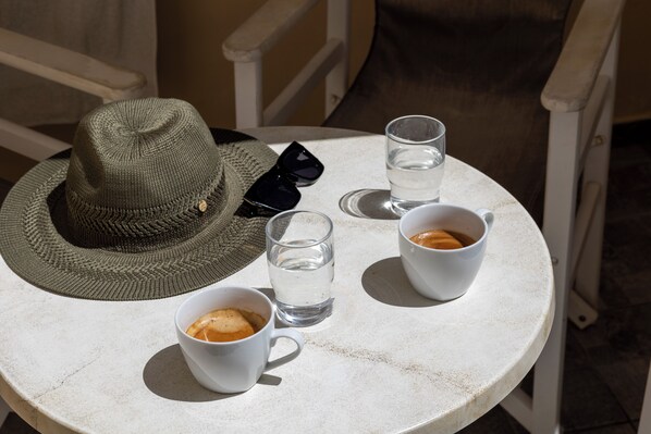 Une table ronde avec un chapeau, deux tasses de café et un verre d’eau.