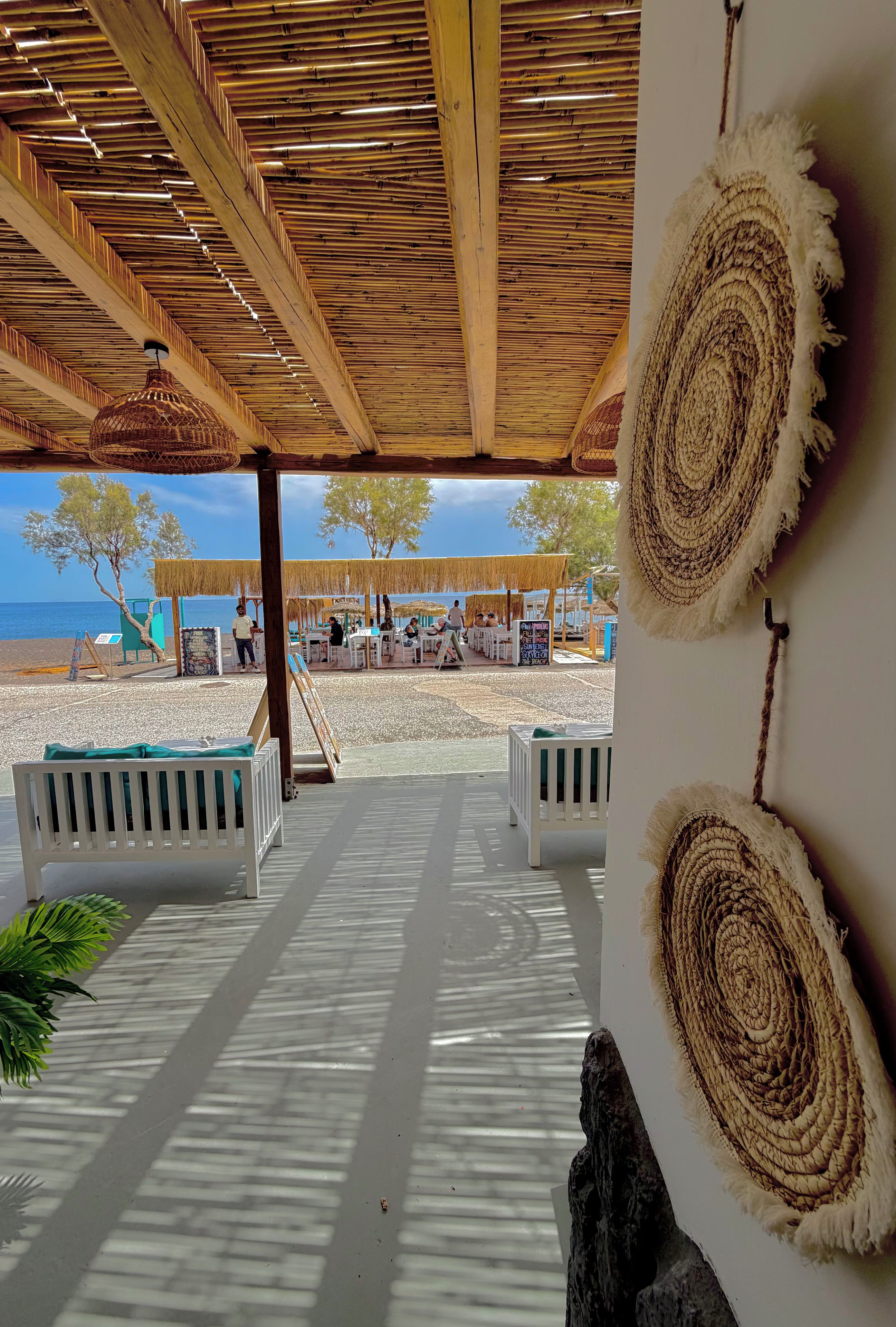 Un patio frente a la playa con vigas de madera, muebles blancos y tapices tejidos.