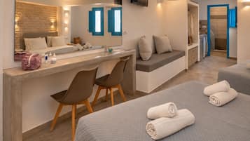 Una habitación de hotel con cama, escritorio con sillas, espejo y baño con ducha.