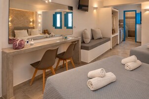 Una habitación de hotel con cama, escritorio con sillas, espejo y baño con ducha.