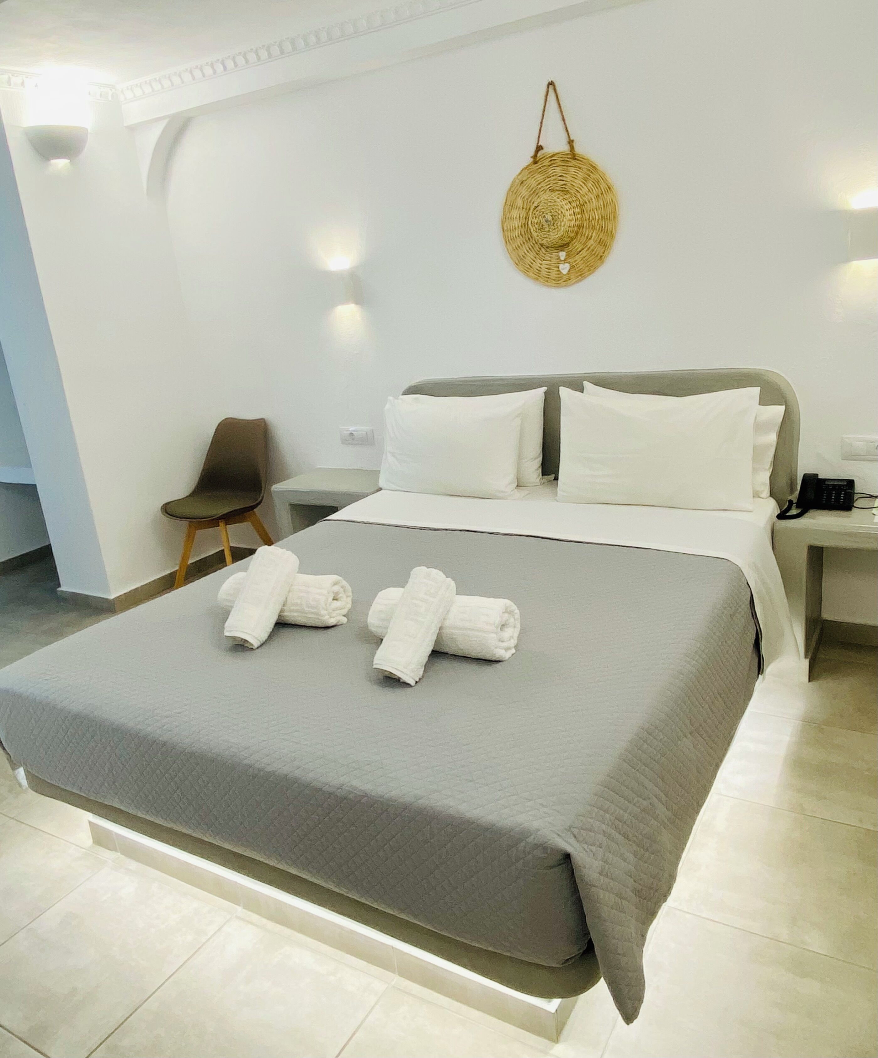 A modern hotel room with a large bed, white linens, a bedside phone, and a wall-mounted light fixture.